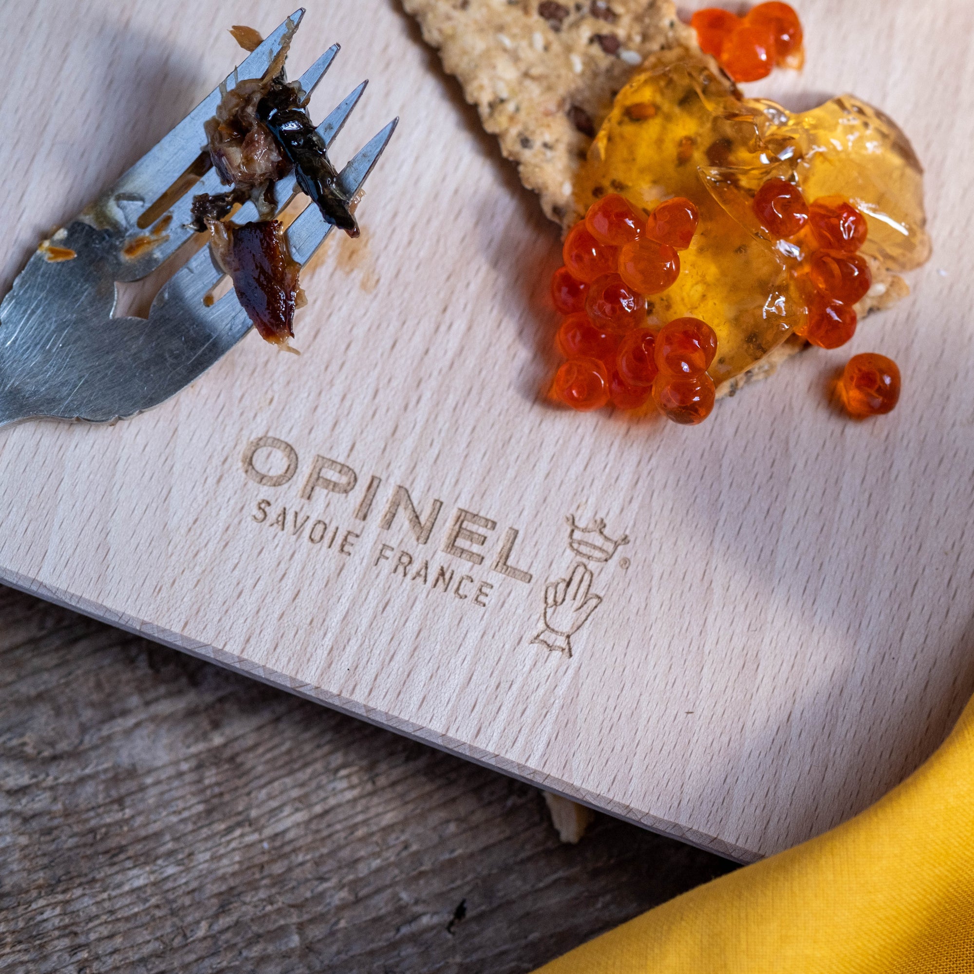 Fork with remnants of fish, orange fish roe on top of jelly on top of a cracker and all on top of an OPINEL SAVOIE FRANCE cutting board