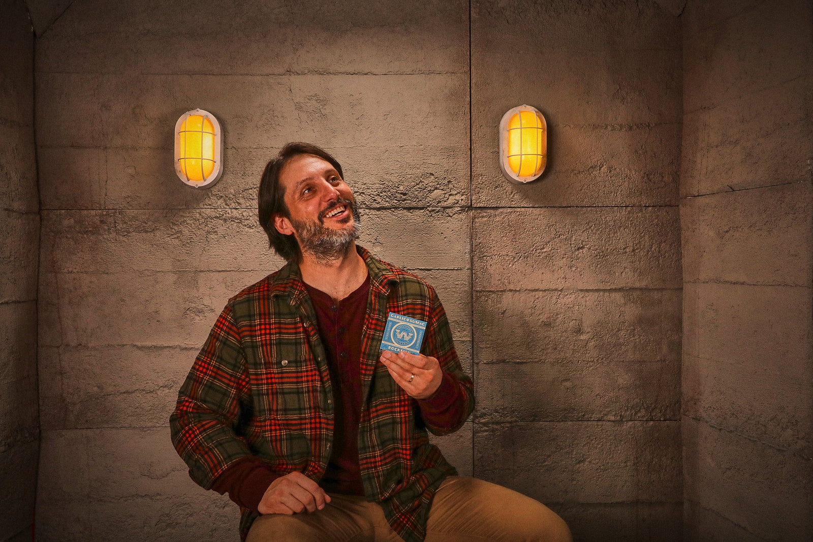 The man grins up at the ceiling, a small blue carton in his hand.
