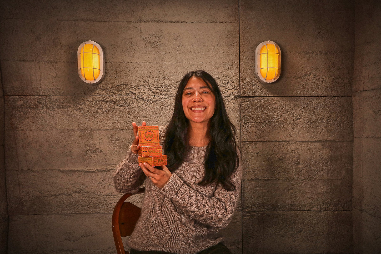 The woman grins at the camera holding an orange Smoked Coho carton.